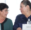 Dos mujeres mayores hablando de frente con una bandera de México al fondo.