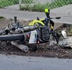 Motocicleta tumbada sobre tierra y hojas al lado de una banqueta con un tenis nike y parte del vehículo a un costado