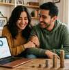 Una pareja en una sal frente a una laptop con gráficas y varias columnas de monedas