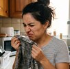 Persona oliendo con asco un trapo de cocina húmedo
