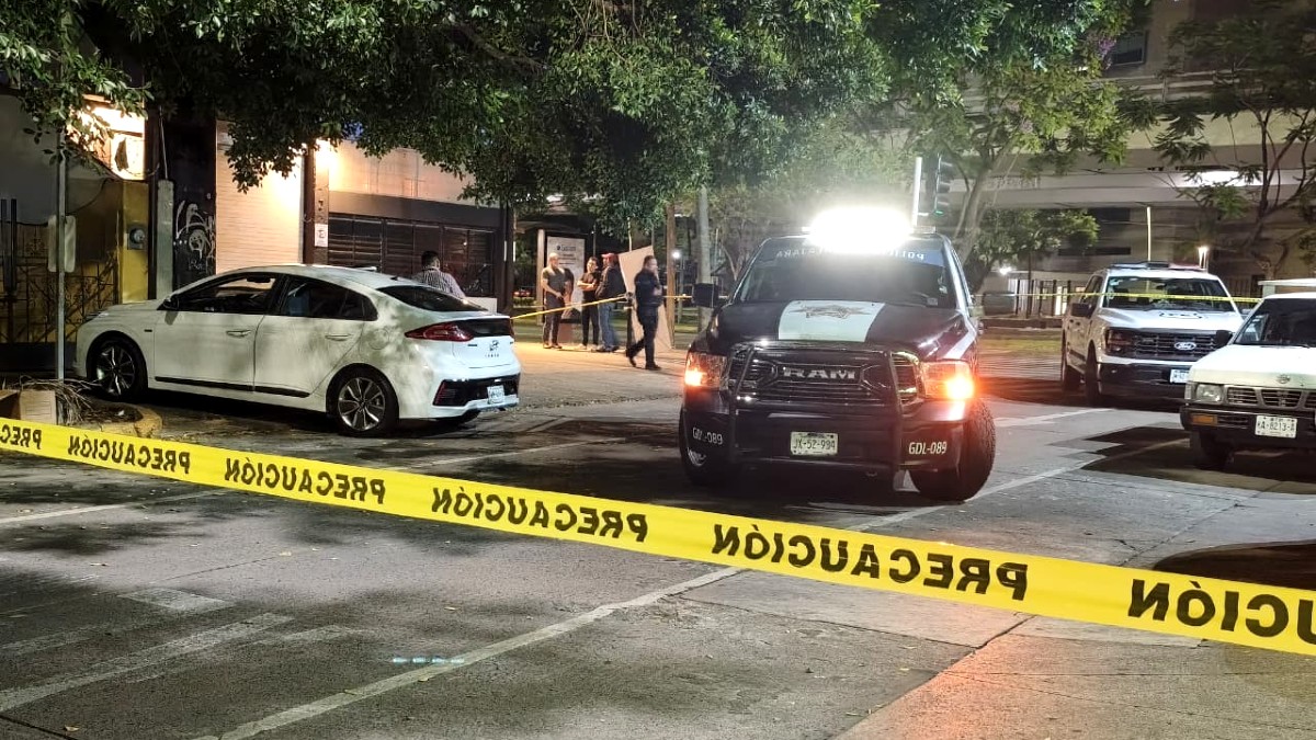 Patrulla de la Policía de Guadalajara detrás de un automóvil Honda color blanco donde se encontró un cuerpo con cintas policiacas acordonando el lugar