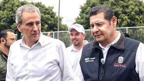 Dos hombres vestidos de manera formal platicando en un parque.