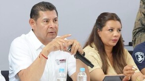 Hombre apuntando al frente con el dedo, sentado junto a una mujer.