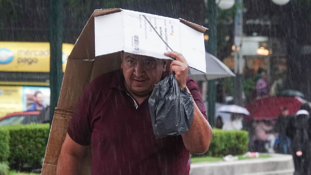 Se observa  a un hombre que se cubre con un cartón ante la lluvia.