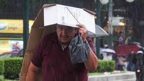 Se observa  a un hombre que se cubre con un cartón ante la lluvia.