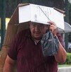 Se observa  a un hombre que se cubre con un cartón ante la lluvia.