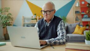 Un adulto mayor usando una computadora portátil en la sala de su casa