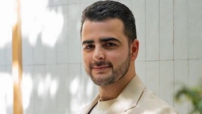 Hombre vestido de traje y con barba posando con una sonrisa para una fotografía.