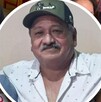 Hombre de playera polo hablando frente a un micrófono junto a la imagen de un hombre adulto con gorra.