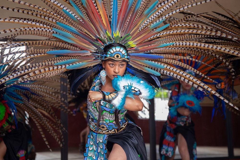 Mujer con traje azteca y penacho realizando una danza.
