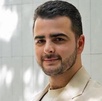 Hombre vestido de traje y con barba posando con una sonrisa para una fotografía.