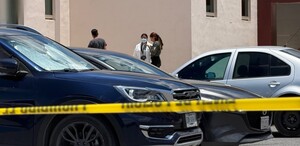 Se observa a uns personas de pie en un estacionamiento; hay una cintilla amarilla de precaución.