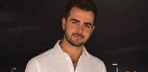 Hombre de barba y camisa blanca sonríe para una fotografía en medio de la noche.