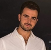 Hombre de barba y camisa blanca sonríe para una fotografía en medio de la noche.