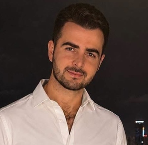 Hombre de barba y camisa blanca sonríe para una fotografía en medio de la noche.