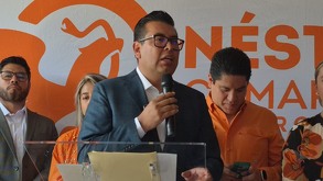 Candidato habla por micrófono y de fondo el logo del partido naranja