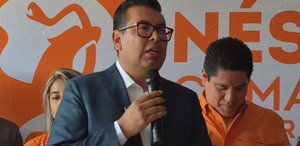 Candidato habla por micrófono y de fondo el logo del partido naranja