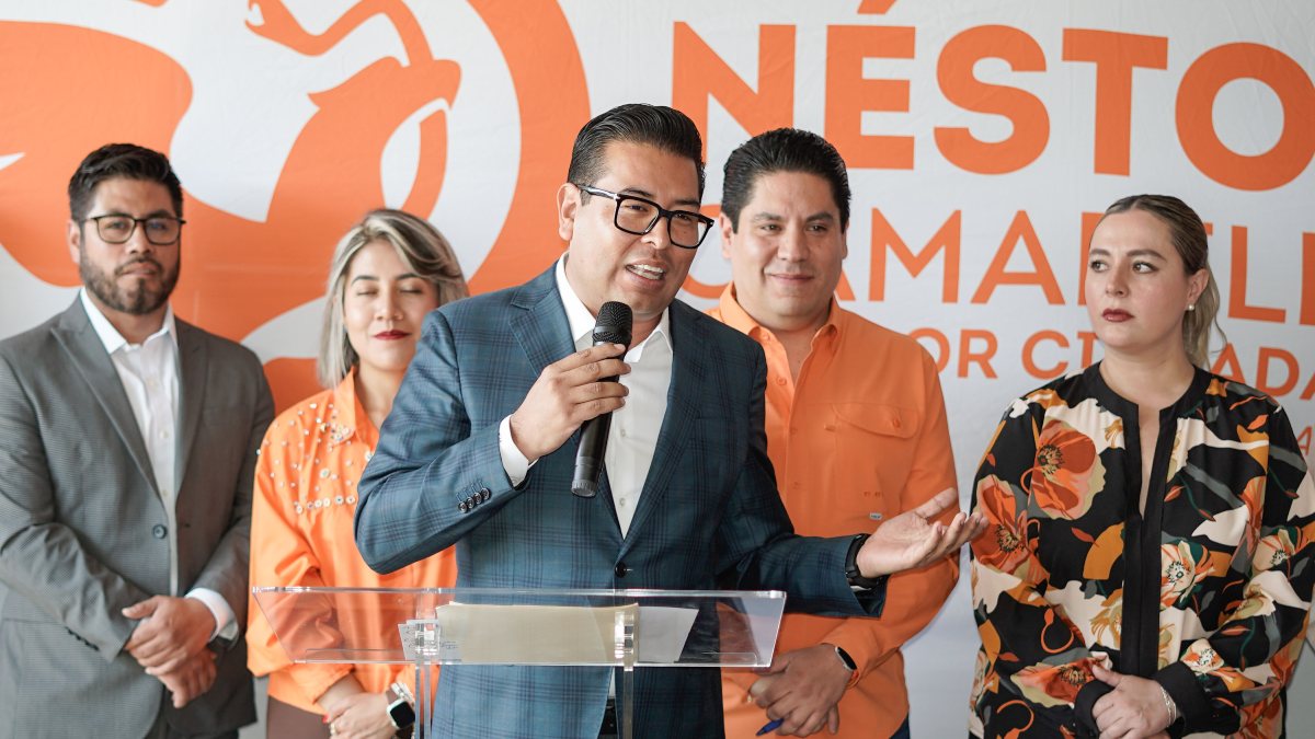 Candidato habla por micrófono en rueda de prensa y de fondo el logo de Movimiento Ciudadano