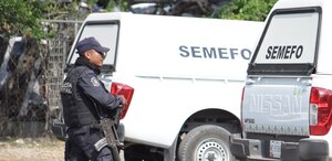 Policía armado caminando junto a una camioneta del Servicio Médico Forense.