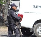 Policía armado caminando junto a una camioneta del Servicio Médico Forense.