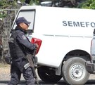 Policía armado caminando junto a una camioneta del Servicio Médico Forense.