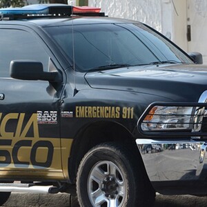 Vista del costado de una patrulla de la Policía del Estado de Jalisco estacionada al exterior de una viviendas con fachada color blanco