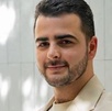 Hombre vestido de traje y con barba posando con una sonrisa para una fotografía.