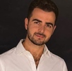 Hombre de barba y camisa blanca sonríe para una fotografía en medio de la noche.
