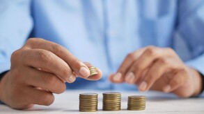 Monedas apoladas en tres columnas y en el fondo un hombre con camisa azul tocando las monedas