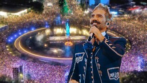 Alejandro Fernández sonriendo mientas sostiene un micrófono con una foto aérea de la Glorieta de La Minerva durante concierto de Maná