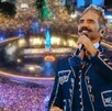 Alejandro Fernández sonriendo mientas sostiene un micrófono con una foto aérea de la Glorieta de La Minerva durante concierto de Maná