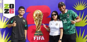Dos hombres y una mujer delante de un cartel promocional del Fan Fest del Mundial en Guadalajara