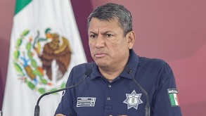 Hombre con traje policiaco hablando ante un micrófono.