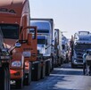 Fila de tráileres estacionados bloqueando una carretera de Jalisco con tres hombres caminando a un costado