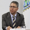 Hombre de traje y lentes sentado junto a una bandera de Puebla.