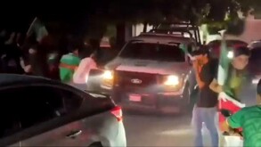 Patrulla de la Policía Municipal de Apatzingán siendo rodeada y empujada por fanáticos con playeras de la Selección Mexicana
