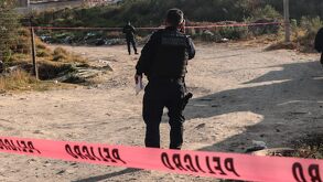 Policía caminando en un paraje cubierto por cintas rojas de advertencia.
