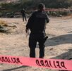 Policía caminando en un paraje cubierto por cintas rojas de advertencia.