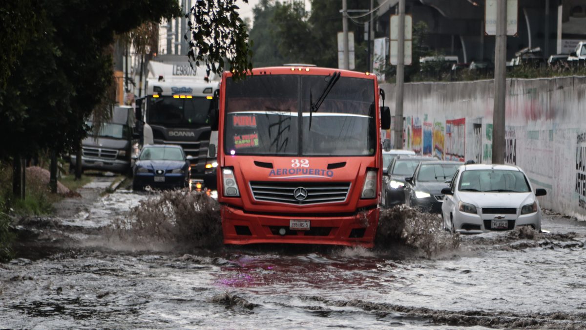 Camión y autos avanzando en una calle inundada por la lluvia en Puebla.