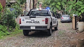 Vista de la parte de atrás de una patrulla de la Policía de Tlaquepaque estacionada en un camino empedrado con un auto enfrente