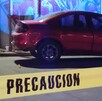 Automóvil color rojo estacionado en la calle al lado de una pared con un grafitti y una cinta policiaca acordonando el sitio