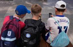 Tres niños utilizan sus celulares sentados en el exterior de una escuela en Sydney, el 8 de diciembre de 2025.