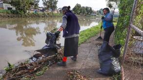 dos mujeres retiran basura de la orilla de una laguna