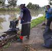 dos mujeres retiran basura de la orilla de una laguna