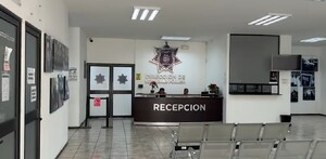 Se observa a dos personas sentadas y hay un escritorio que dice Recepción.