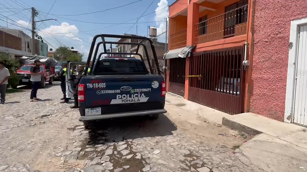 Vista de la parte trasera de una patrulla de la Policía de Tonalá con policías y personas al exterior de una casa acordonada tras un incendio