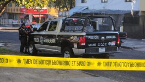 Patrulla de la Policía de Guadalajara con policías apoyados en el cofre dentro de un área acordonada por una cinta policiaca amarilla
