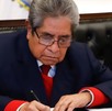 Hombre anciado de traje y lentes firmando un documento.