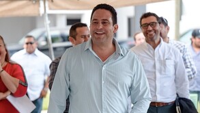 Se observa a un hombre sonriendo que viste una camisa azul celeste.
