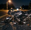 Se observa una motocicleta color negra, está destrozada y en una carretera; es de noche.